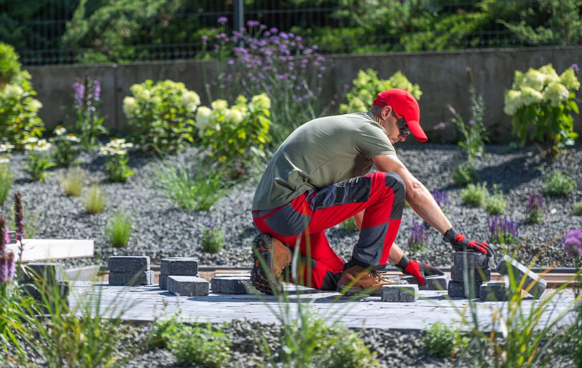 Gardener laying gray paving stones in a landscaped backyard designed by Lee's Landscaping