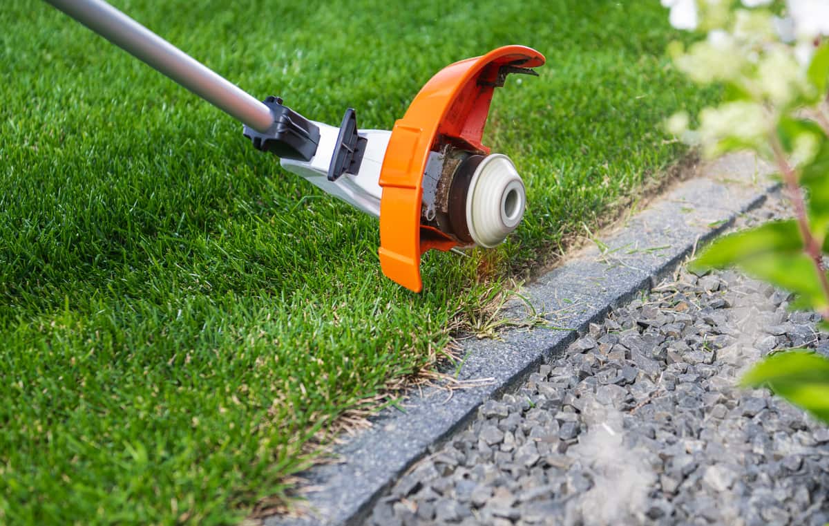 A well-maintained backyard garden with grass being trimmed along a stone border by Lee's General Landscaping