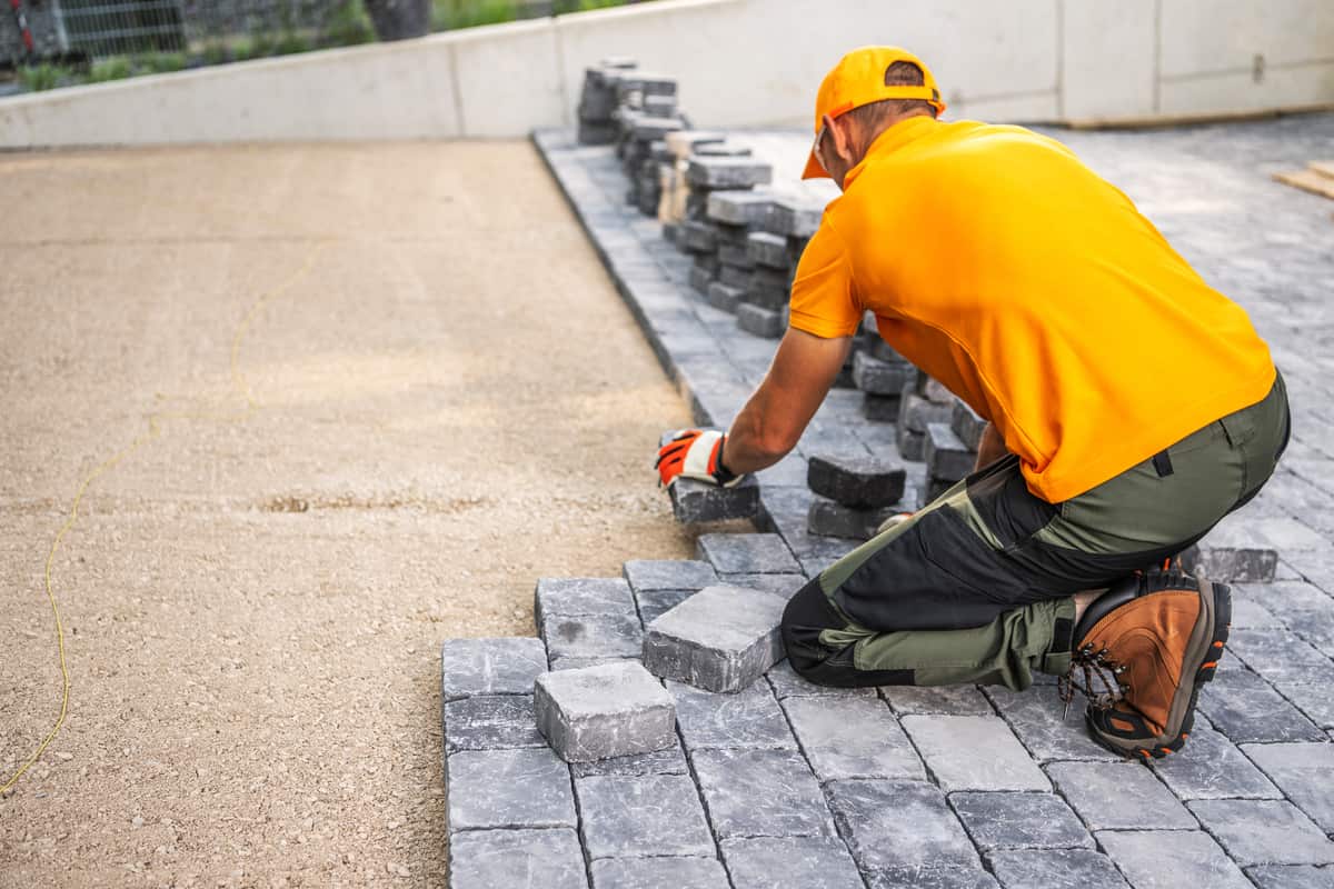 Worker laying cobblestones for a patio by Lee's General Landscaping